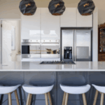 Modern kitchen featuring a large island with white stools, sleek cabinetry, stainless steel appliances, and stylish pendant lights.