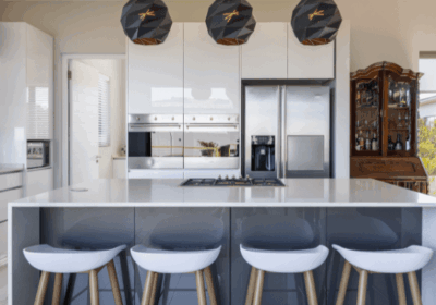 Modern kitchen featuring a large island with white stools, sleek cabinetry, stainless steel appliances, and stylish pendant lights.