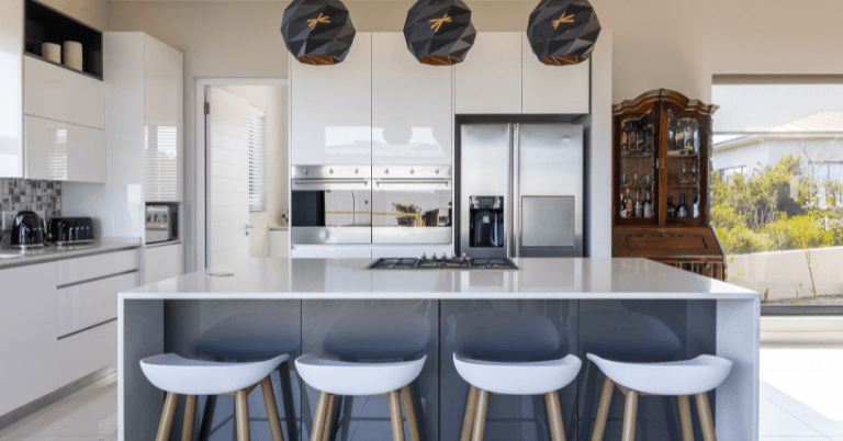 Modern kitchen featuring a large island with white stools, sleek cabinetry, stainless steel appliances, and stylish pendant lights.